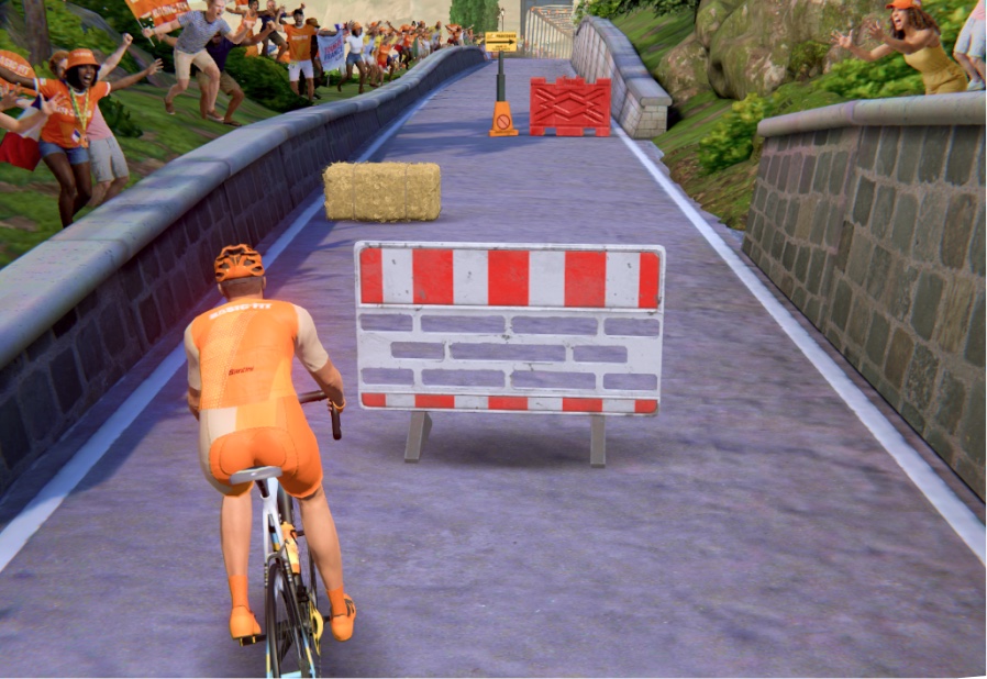 A Basic-Fit rider swerving around a red-and-white road-block on a bridge climb, crowds cheering from the roadside