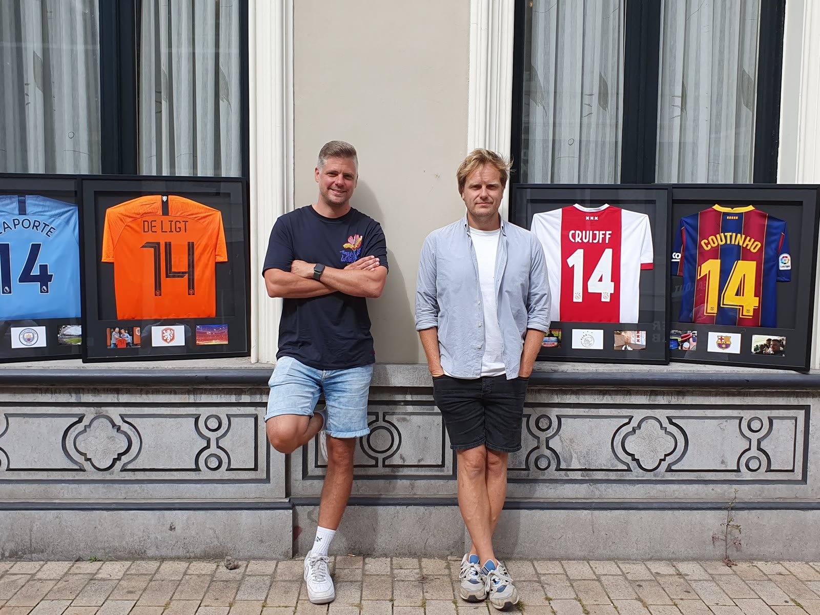 Founders Erik van Mourik and Frits Mahovic in front of framed club shirts